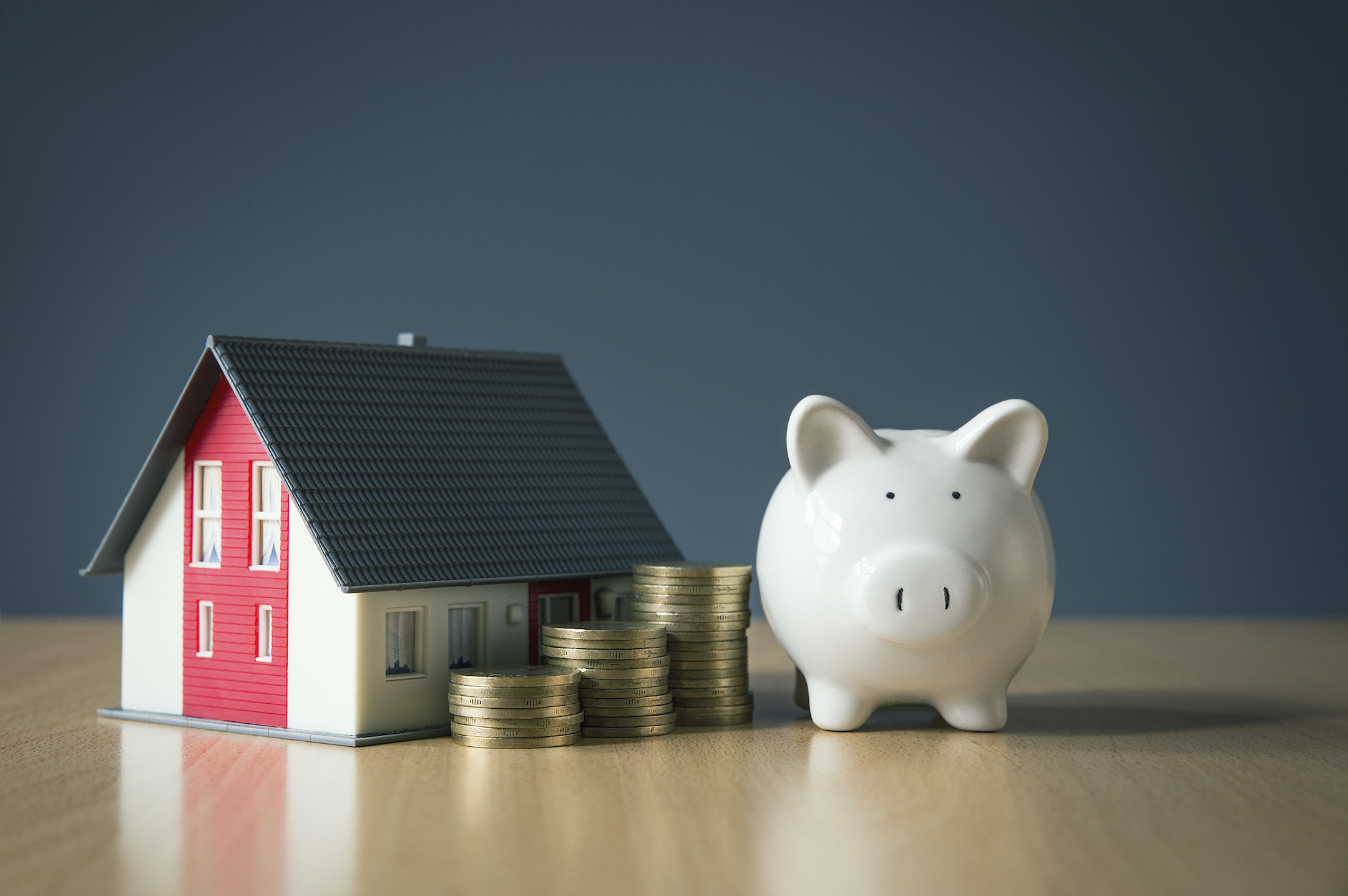 A piggy bank is sitting on a table with coins stacked by a miniature house to showcase home equity loan nj.