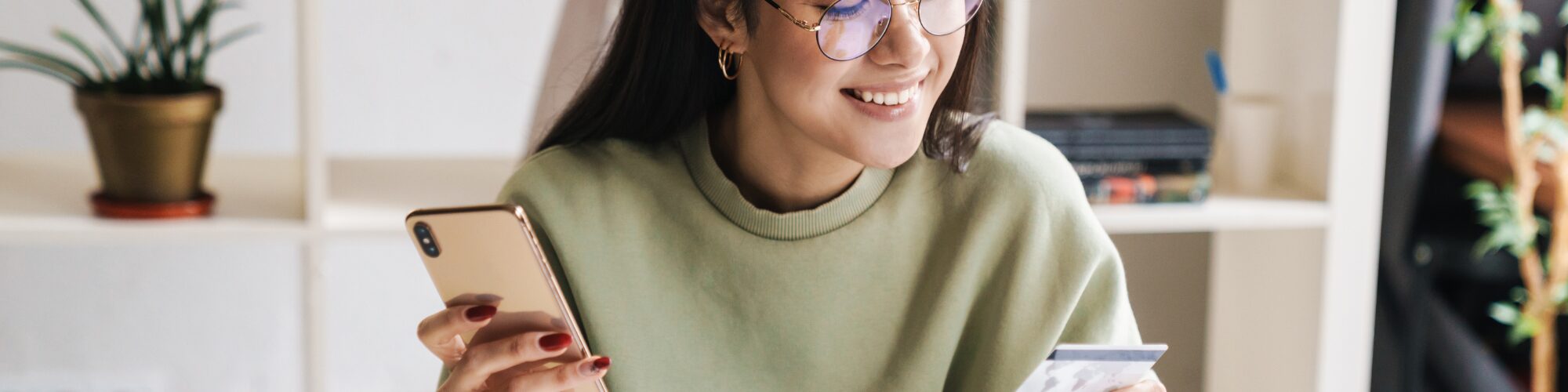 a woman in a green sweater using her bank card on her cell phone